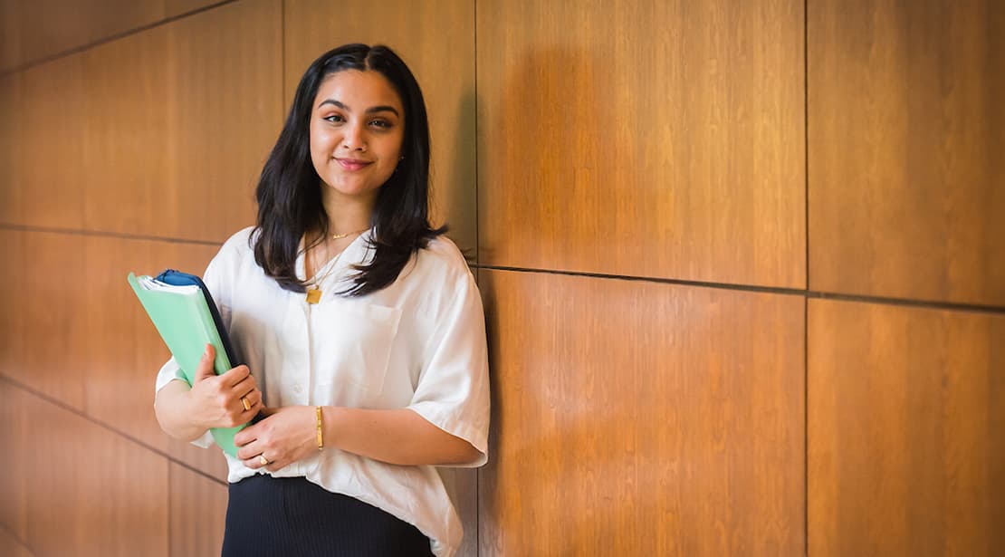 Student in hallway, holding books and smiling