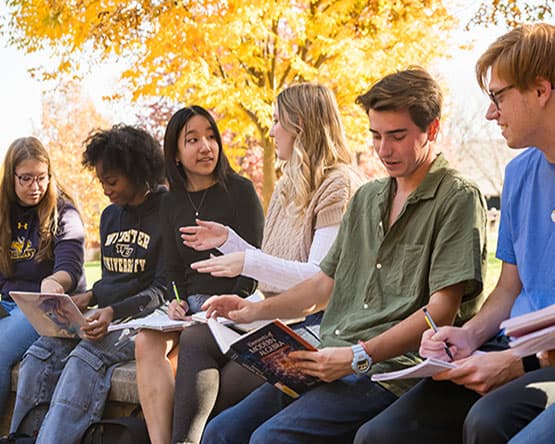 Students outside sitting on a wall, talking.
